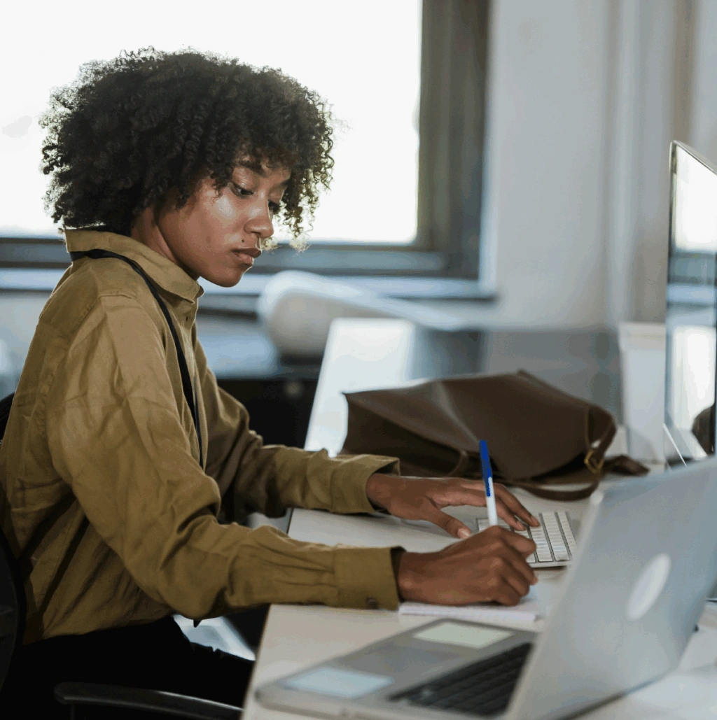 Young professional working at a laptop by a bright window, focused on typing