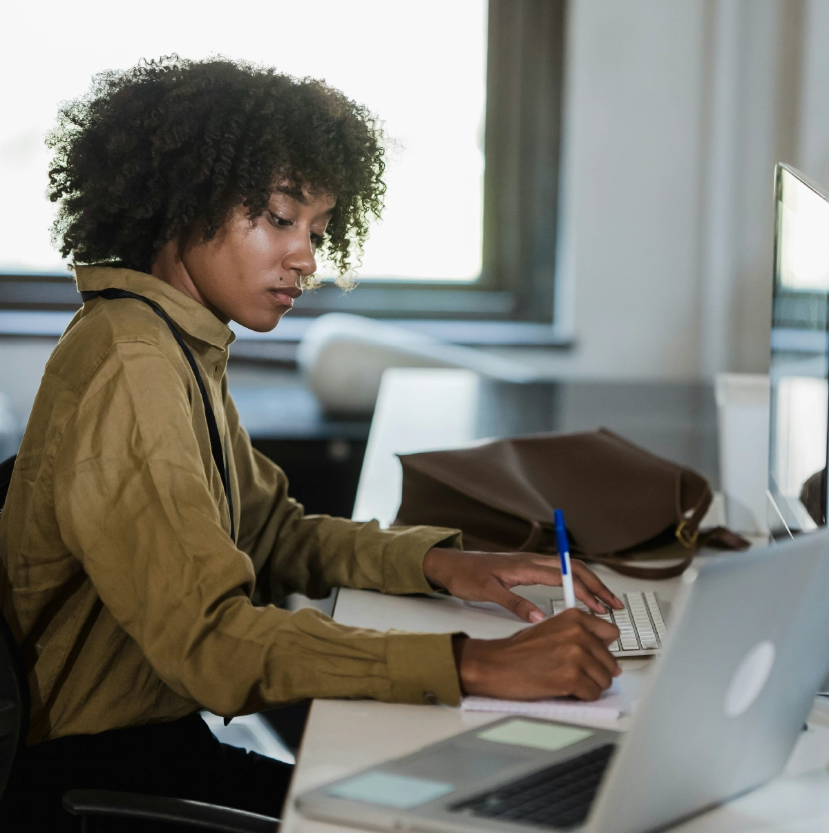 Young professional working at a laptop by a bright window, focused on typing