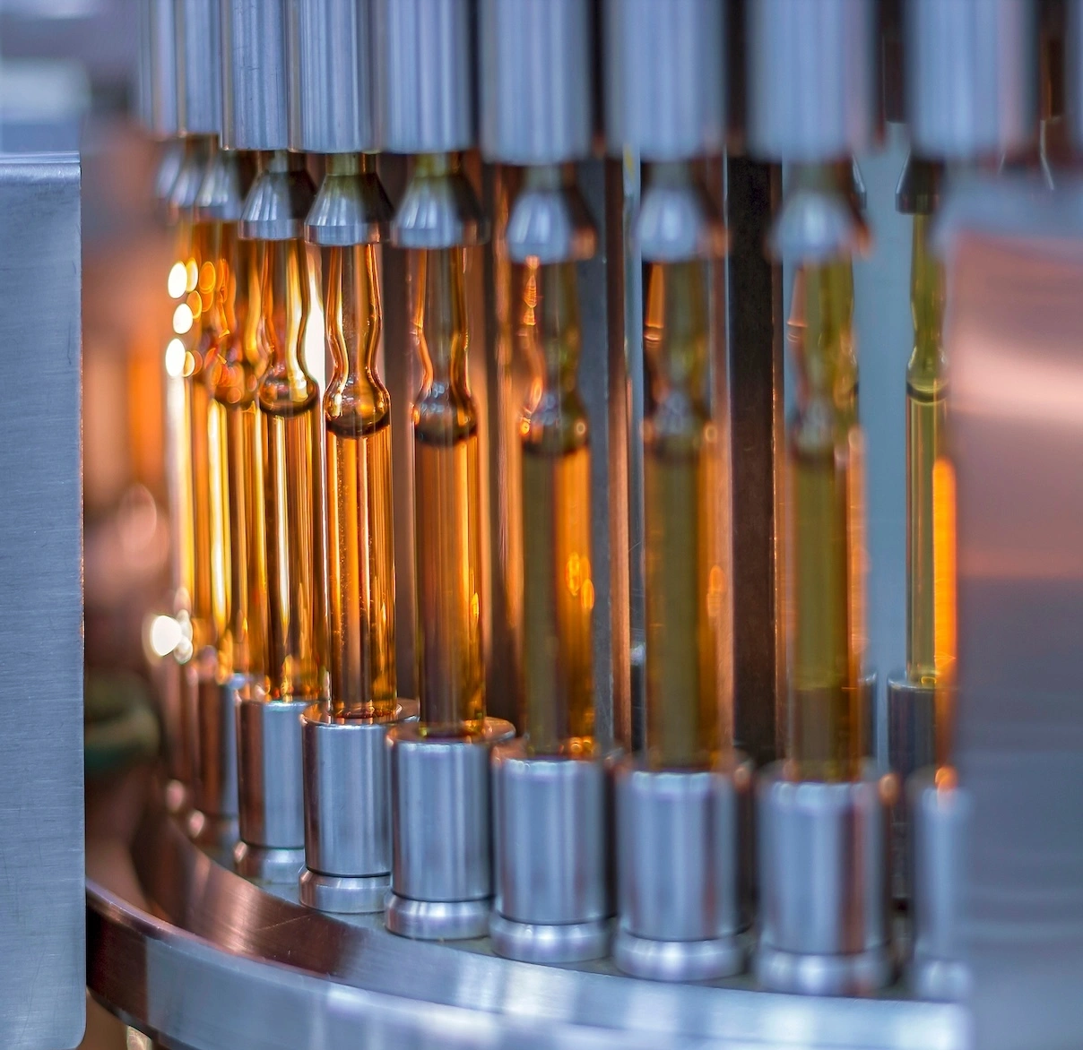Row of amber glass bottles filled with liquid on a stainless steel bottling machine in an industrial setting.