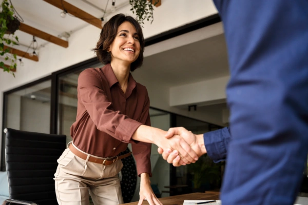 Woman of color shaking hands in a boardroom with another person out of frame.